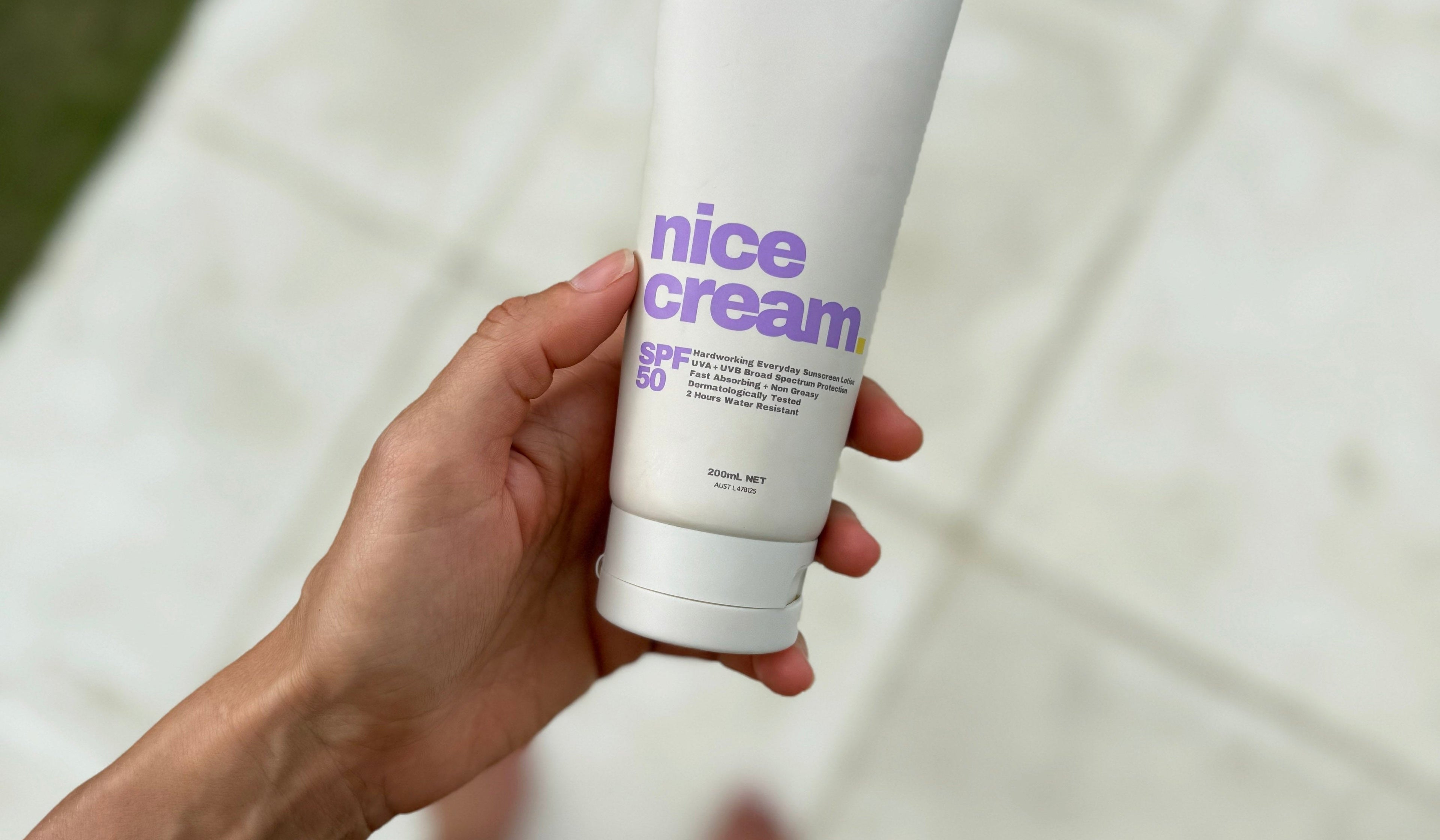Hand holding a tube of 'nice cream' on a white surface with a blurred background